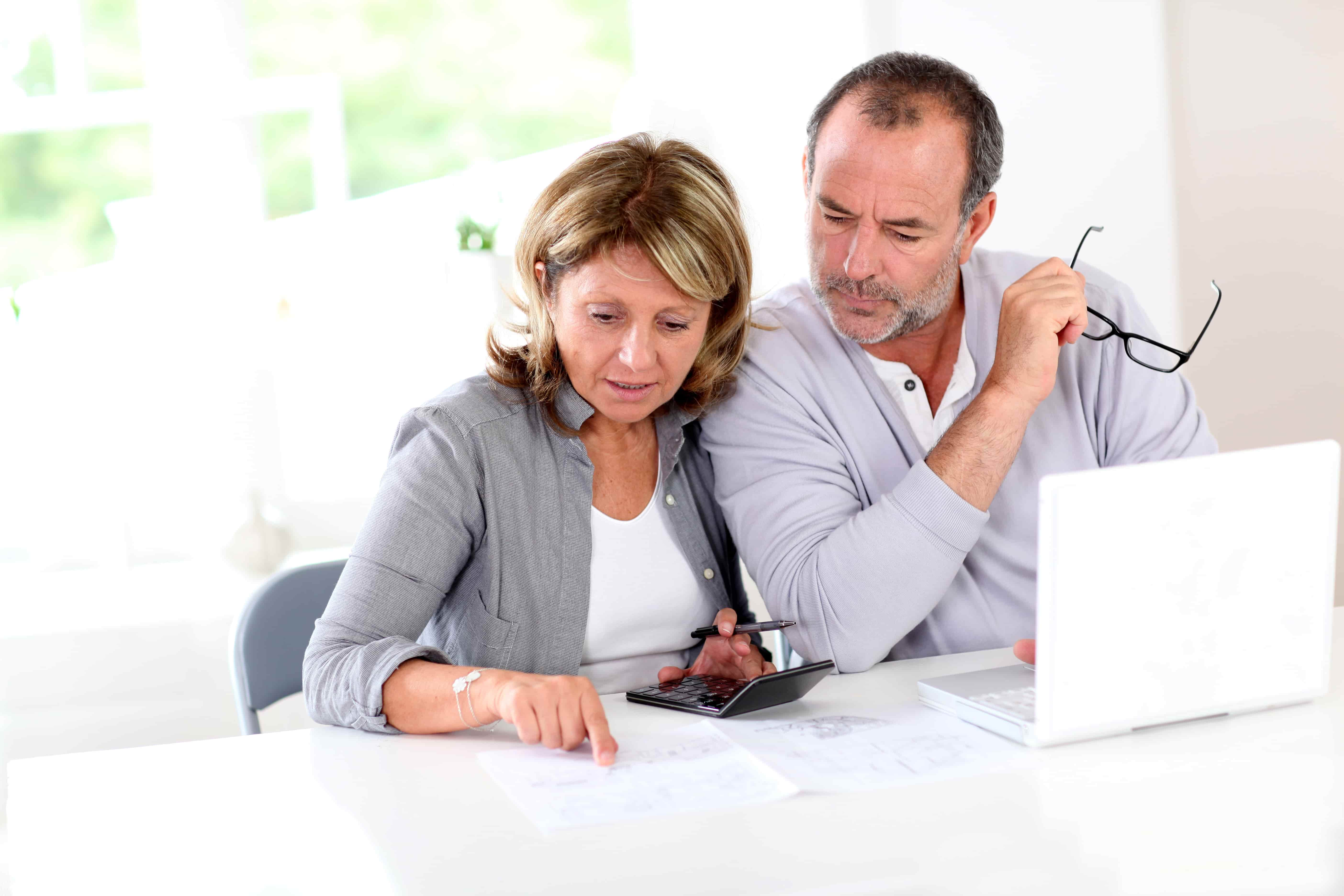 Couple reading retirement plan at home with use of laptop